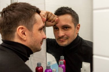 Siyah balıkçı yaka giyen ve aynaya bakan kısa saçlı genç bir adamın portresi. Aynaya bakan genç bir adamın yansıması..