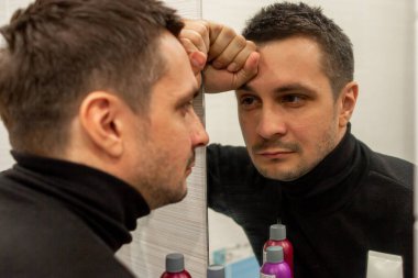 Siyah balıkçı yaka giyen ve aynaya bakan kısa saçlı genç bir adamın portresi. Aynaya bakan genç bir adamın yansıması..