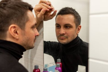 Siyah balıkçı yaka giyen ve aynaya bakan kısa saçlı genç bir adamın portresi. Aynaya bakan genç bir adamın yansıması..