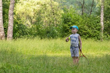 24.06.2020, Maloyaroslavets. - Rusya. Ormandaki çayırda büyük tenis oynayan küçük bir çocuk..