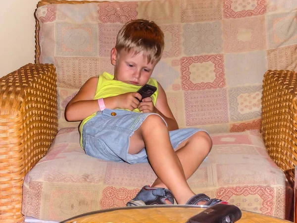 Ένα Ξανθό Αγόρι Που Κάθεται Στην Πολυθρόνα Και Παίζει Τηλέφωνο — Φωτογραφία Αρχείου