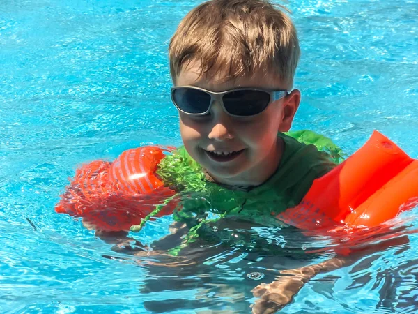 2012年9月18日 埃及Hurghada 一个可爱的小男孩 戴着蓝色的旗袍 戴着红色的充气臂章 在游泳池里学习游泳 — 图库照片