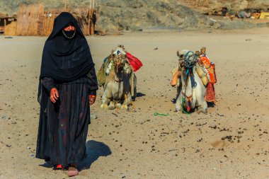 17.09.2012, Hurghada, Mısır. Bedevi kadın, siyah elbiseli, yalancı devenin yanında duruyor. Afrika 'nın yerlileri.