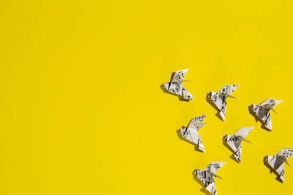 Flock of flying origami doves on yellow background. Sheet music paper origami birds. Concept of festive music postcard.