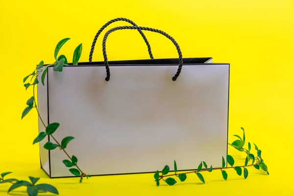White paper bag and climbing plant on yellow background.