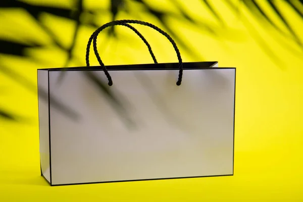 White paper bag and palm tree leaf on yellow background. Concept of shopping.