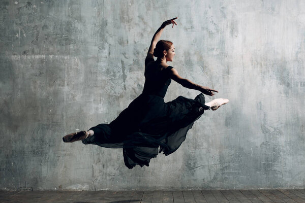 Прыжок балерины. Молодая красивая балетная танцовщица, одетая в профессиональный костюм, пуанты и черное платье
.