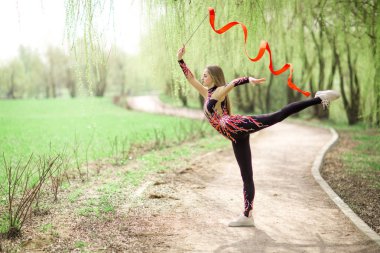 Ritmik jimnastik. Parkta kırmızı kurdele açık genç jimnastikçi kız