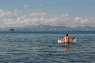 Genç bir adam dağlar zemin karşı denizde yüzüyor