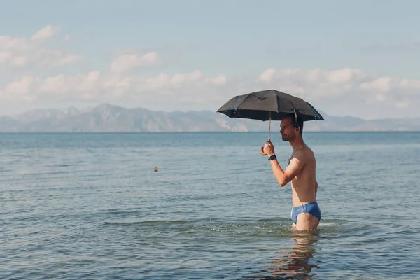 Young man swims with an umbrella in the sea