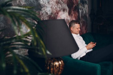 Cep telefonu ile yeşil kanepe oturan beyaz gömlekli bir işadamıportresi. İş ve başarı kavramı.