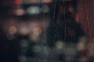 Akşamları pencere camında yağmur damlaları. Şehir, ışıklar ve yağmur.