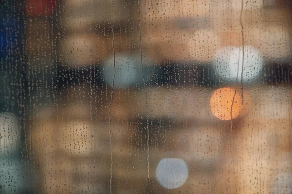 Raindrops on a window glass in the evening. City, lights and rain.
