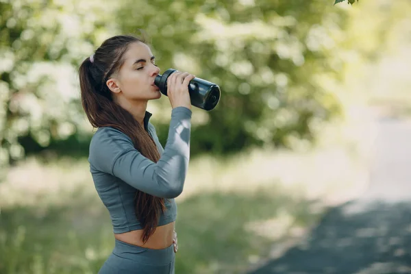 Sportos nő palackozott vizet iszik a parkban. — Stock Fotó