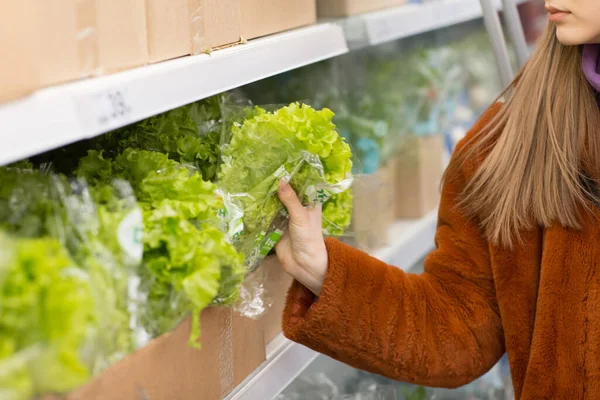 Jovem com uma cesta de supermercado escolhe produtos no departamento de vegetais. Salada verde — Fotografia de Stock