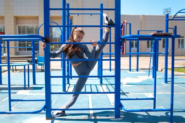 Joven mujer delgada haciendo cordel para estirar las piernas. Chica positiva haciendo las divisiones al aire libre. — Foto de Stock