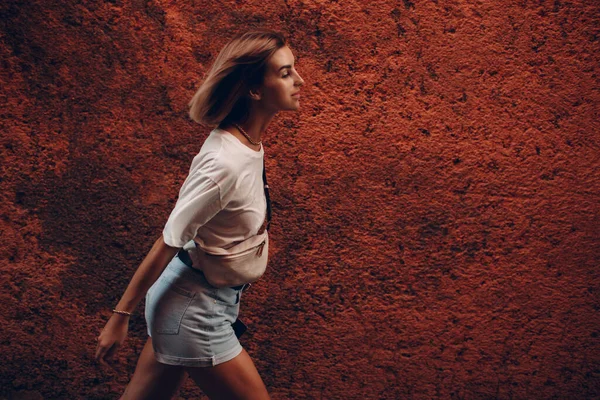 Молодая женщина целенаправленно идет вперед. Девушка в повседневной одежде идет против красной каменной стены в Марракеше, Марокко — стоковое фото