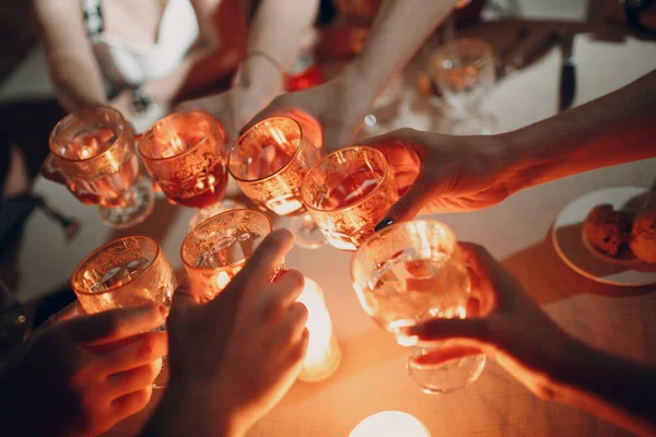 Mãos a segurar os copos com uma bebida a fazer um brinde na festa. Foco suave e vela acesa no fundo — Fotografia de Stock