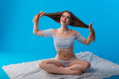 Mavi arka planda izole edilmiş beyaz çizgili mayo giymiş komik duyguları olan genç bir kadın.