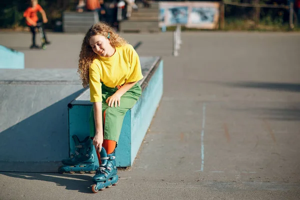 Молода дівчина в зеленому і жовтому одязі збирається роликові ковзани — стокове фото