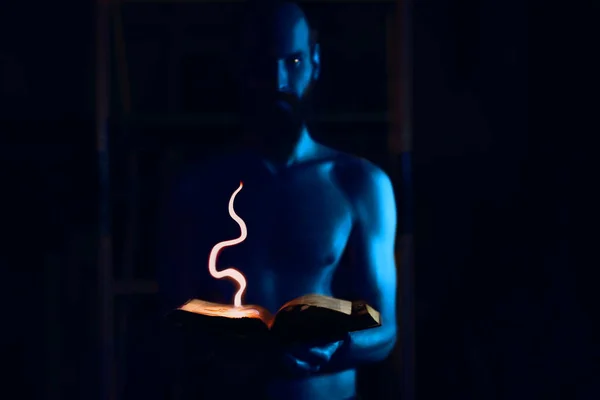 Muž čaroděj s modrou pletí drží v rukou hořící knihu kouzel — Stock fotografie