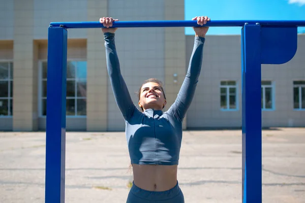 Menina fazendo exercícios na barra horizontal ao ar livre. Jovem no treino. — Fotografia de Stock