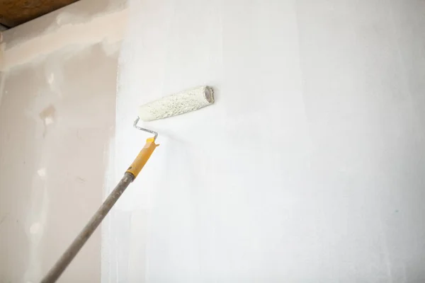Rodillo de pintura blanco en mano con pared de paneles de yeso — Foto de Stock