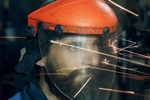 Człowiek w przezroczystej masce ochronnej pracuje na metalu z piłą tarczową. Iskry i twarz. — Zdjęcie stockowe