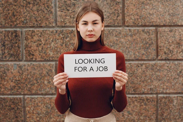 Giovane donna tenere poster di carta bianca in mano. Ragazza con foglio bianco modello vuoto con iscrizione Alla ricerca di un lavoro. — Foto Stock