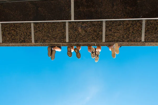 Anak laki-laki kaki di sepatu tergantung dari jembatan terhadap langit biru — Stok Foto