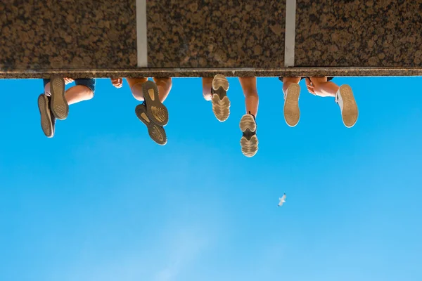 Garçons jambes dans des chaussures suspendues au pont contre le ciel bleu — Photo