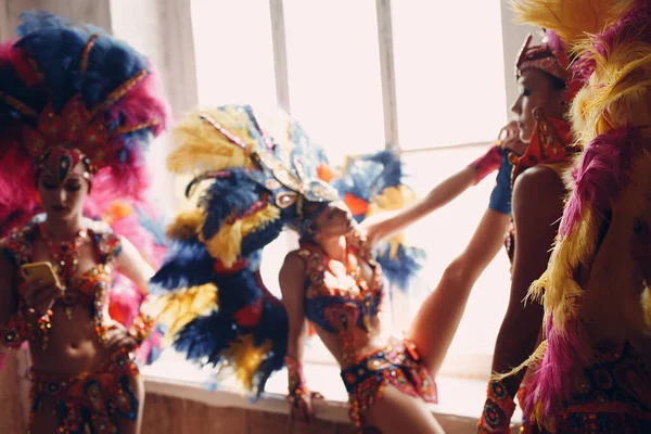 Mujer en traje de carnaval de samba brasileña con plumaje de plumas de colores relajarse en la antigua entrada con ventana grande —  Fotos de Stock