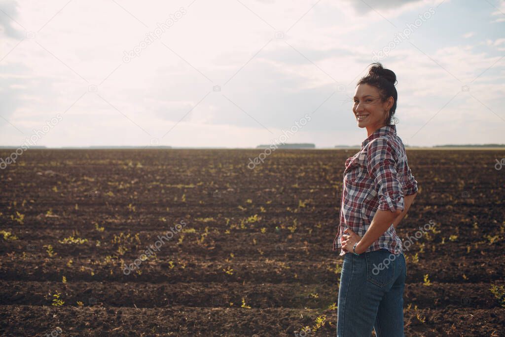 Woman farmer standing and looking agricultural field soil