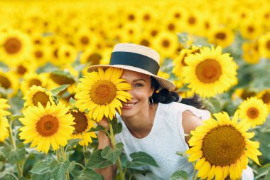 Güzel, gülümseyen, şapkalı bir kadın. Gözünde çiçek, yüzünde de ayçiçeği tarlası.