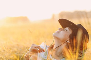 Kovboy şapkalı kadın portresi. Gün batımında tarım tarlasında kulağıyla.