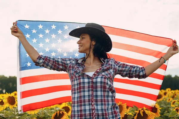 Νεαρή γυναίκα με αμερικανική σημαία στο χωράφι με τα ηλιοτρόπια. 4η Ιουλίου Ημέρα Ανεξαρτησίας ΗΠΑ έννοια. — Φωτογραφία Αρχείου