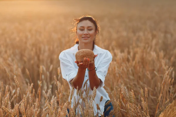 Donna che tiene il pane di grano fatto in casa nelle mani nel campo di grano al tramonto. — Foto Stock