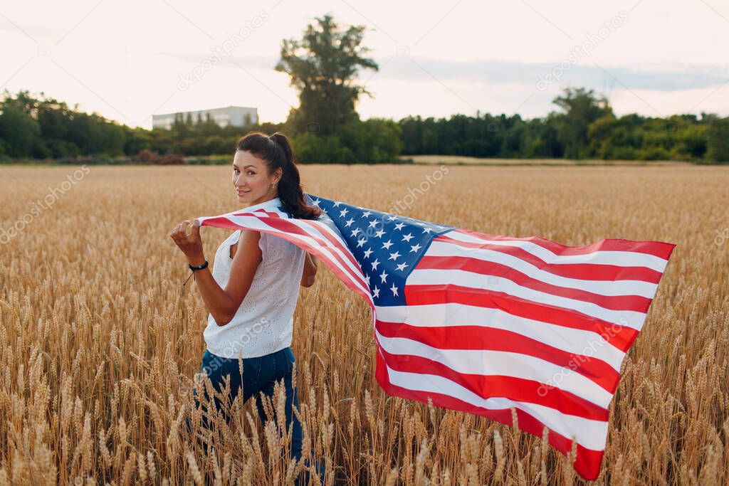 Woman with American flag in wheat field at sunset. 4th of July. Independence Day patriotic holiday.