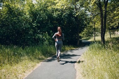 Şehir parkında koşan kız. Genç bayan koşucu dışarıda koşuyor. Arka plan.