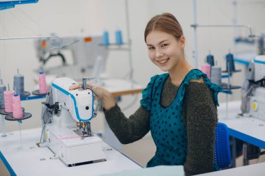 Genç, güzel terzi fabrikadaki dikiş makinesine dikiş dikiyor.