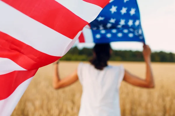 Femeie cu steag american în câmp de grâu la apusul soarelui. 4 iulie. Ziua Independenței sărbătoare patriotică . — Fotografie, imagine de stoc
