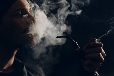 Siyah arka planda pipo içen bir adam. Arka ışıklandırılmış profil portresi.