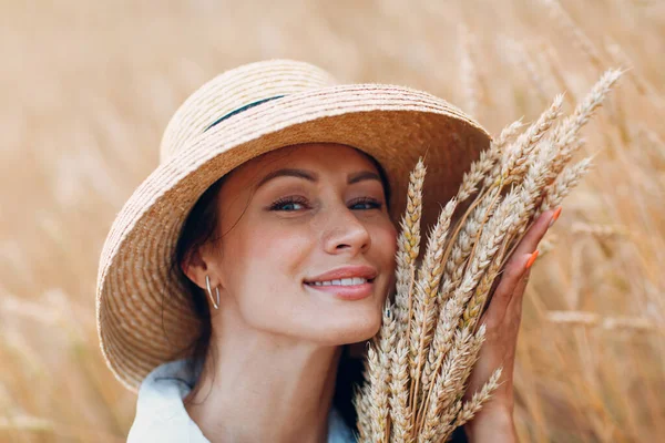 Giovane donna in cappello di paglia che tiene covone di spighe di grano in campo agricolo — Foto Stock