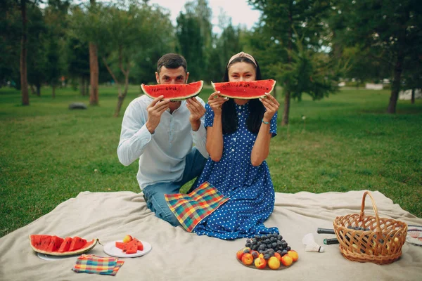 Mladý dospělý žena a muž pár piknik na zelené travnaté louce v parku se baví a úsměv s melounem — Stock fotografie