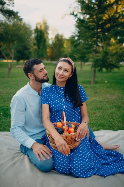 Jovem mulher adulta e homem casal piquenique sentado com frutas cesta no prado de grama verde no parque. — Fotografia de Stock