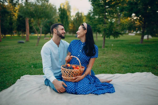 Mujer adulta joven y hombre pareja picnic sentado con frutas cesta en prado de hierba verde en el parque. — Foto de Stock