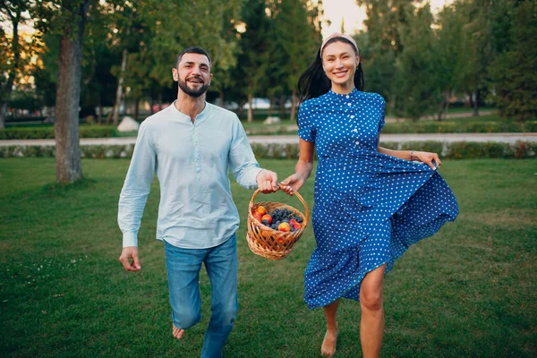 Glückliches Paar mit Früchten im Picknickkorb beim Laufen im Park. — Stockfoto