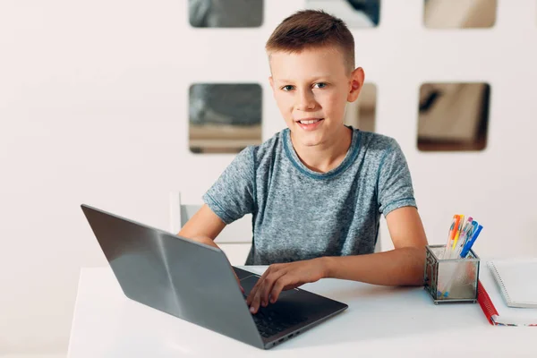 Νεαρό αγόρι κάθεται στο τραπέζι με φορητό υπολογιστή και ετοιμάζεται για το σχολείο στο σπίτι. Έννοια ηλεκτρονικής εκπαίδευσης. — Φωτογραφία Αρχείου