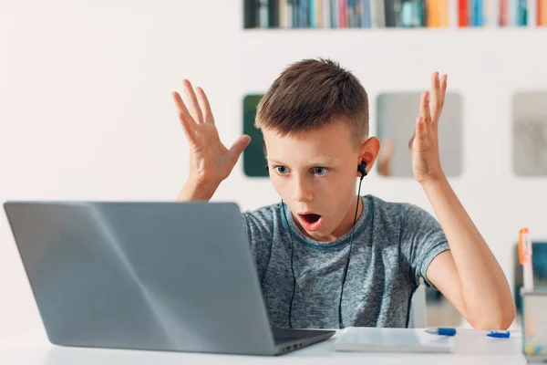 Νεαρό αγόρι σε ακουστικά κάθεται στο τραπέζι με φορητό υπολογιστή και ετοιμάζεται για το σχολείο. Έννοια ηλεκτρονικής εκπαίδευσης. — Φωτογραφία Αρχείου