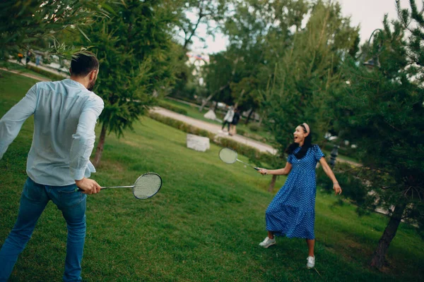 Genç bir çift parkta badminton oynuyor.